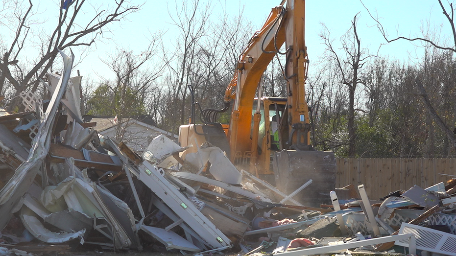 A crane operator lifts a pile of rubble from a demolished house