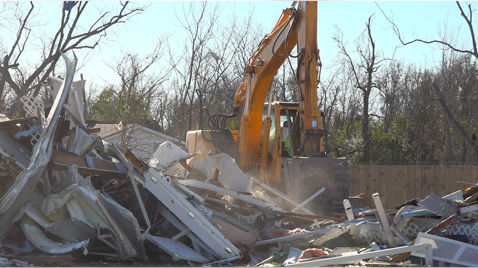 A crane operator lifts a pile of debris from a torn-down home