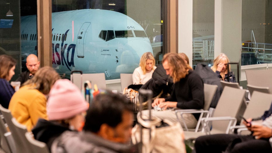 Travelers wait in the terminal as an Alaska Airlines plane sits at a gate at Los Angeles International Airport in Los Angeles, on January 11, 2023