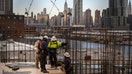 A general view shows construction workers standing before the Manhattan skyline and Empire State Building, in Brooklyn on January 24, 2023. (Photo by Ed JONES / AFP) (Photo by ED JONES/AFP via Getty Images)