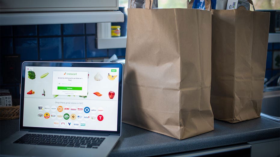 Laptop opened to Instacart with grocery bags on the counter.