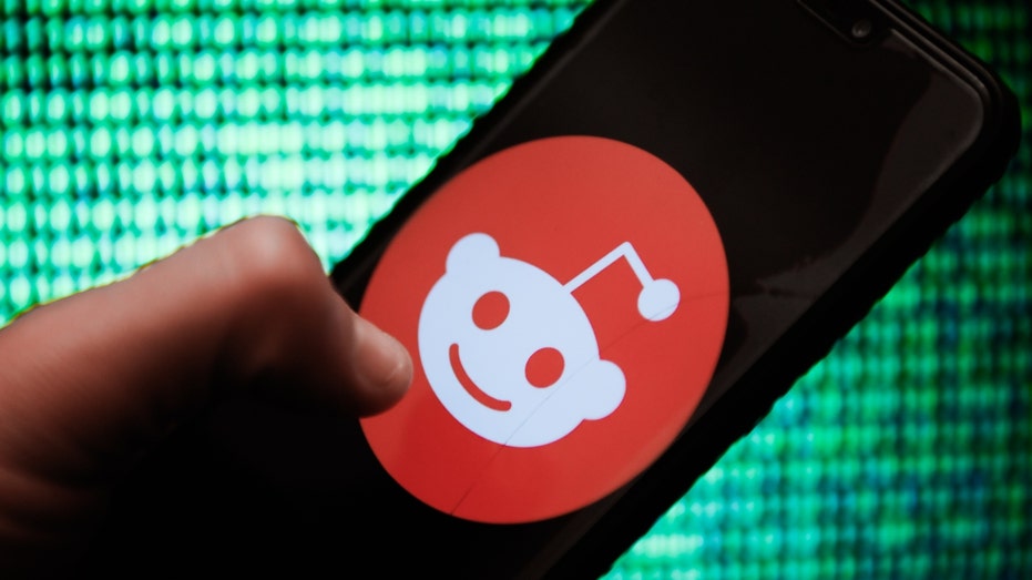 A person holds a phone with the Reddit logo