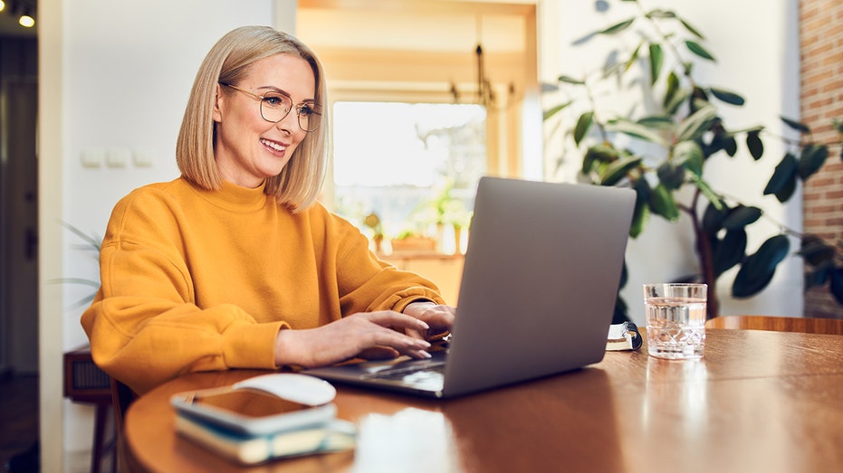 A woman sits at home working on her laptop computer.