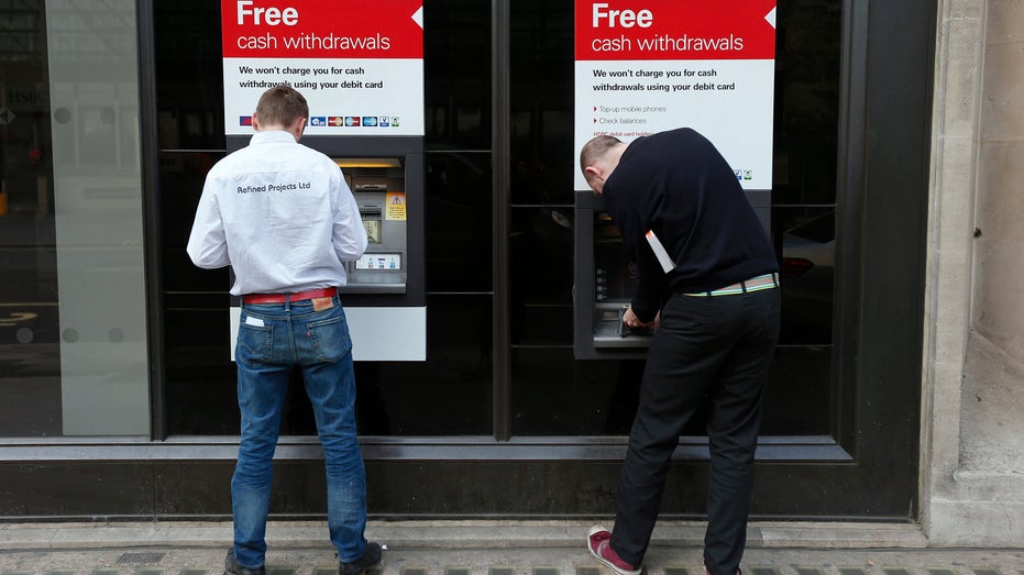 Two men use automated teller machines outside a HSBC bank in London