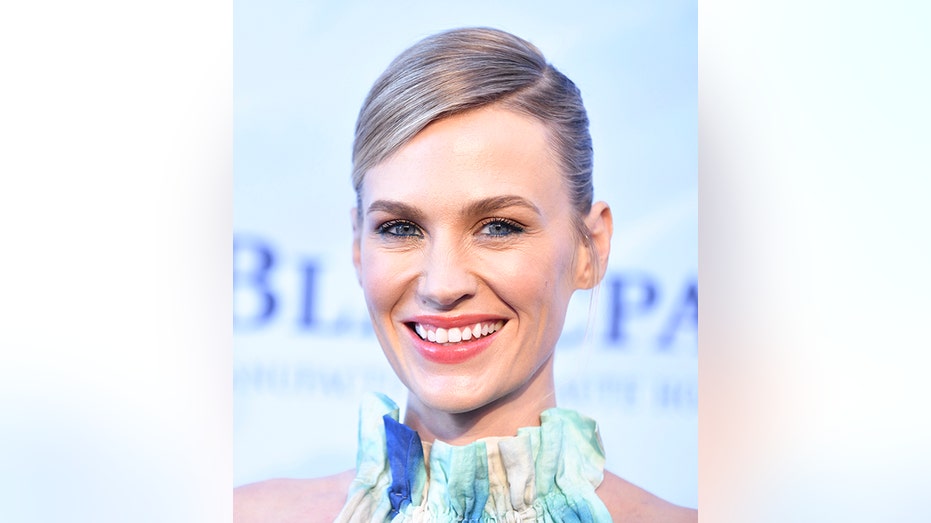 January Jones with slicked back hair smiles on the red carpet in a halter dress with blues and greens and oranges