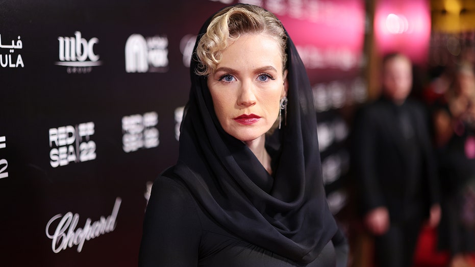 January Jones with a bold red lip stares directly at the camera in a black hooded dress