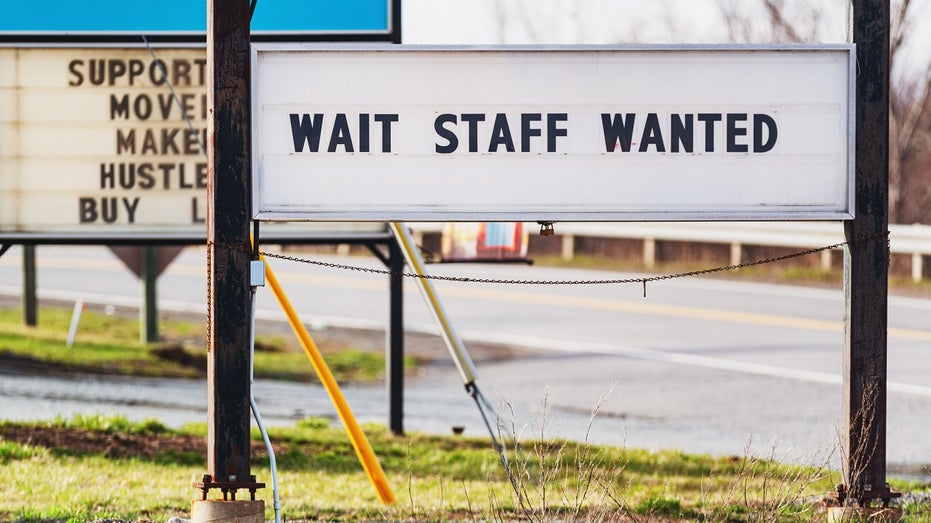 A sign outside a restaurant says 'wait staff wanted'
