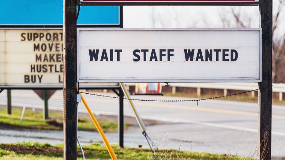 A sign outside a restaurant says 'wait staff wanted'