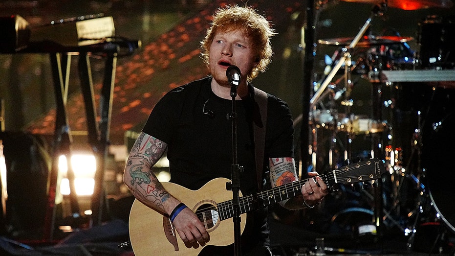 Ed Sheeran in a black t-shirt plays guitar and sings on stage in Los Angeles