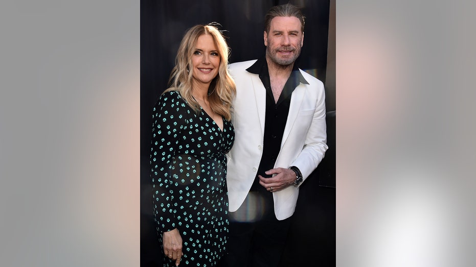 John Travolta wearing a three-piece suit next to his wife Kelly Preston in a black and blue polka dot dress