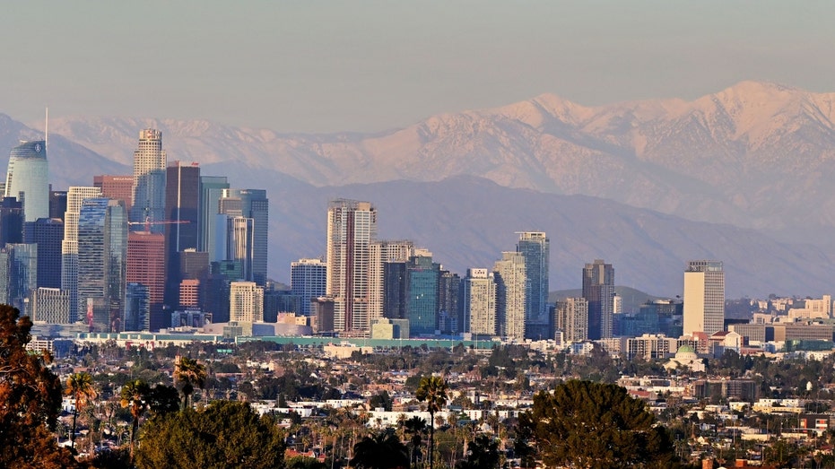 Snow-capped mountains are seen in the distance behind the Los Angeles skyline