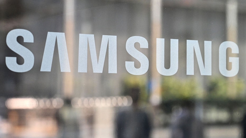 People walk past the Samsung logo on a glass door
