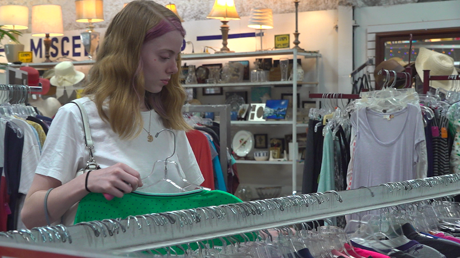 Young woman browsing clothes on a sale rack. Holding green shirt