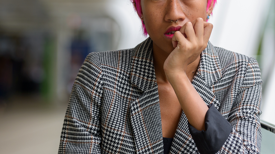 Distress woman with short pink hair stops to think in public space.