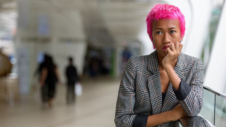 Distressed woman with short pink hair stops to think in public space.