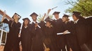 Students smile and wave diplomas after their college graduation.