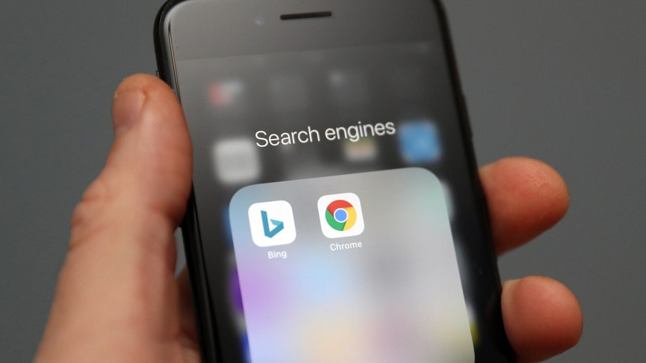 A person holds an iPhone showing the apps for Bing and Google Chrome