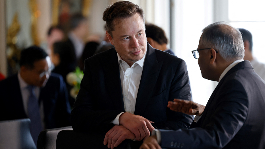 Elon Musk dressed in a suit discussing matters with another CEO