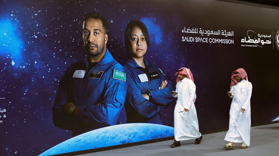 Saudis walk past poster of astronauts