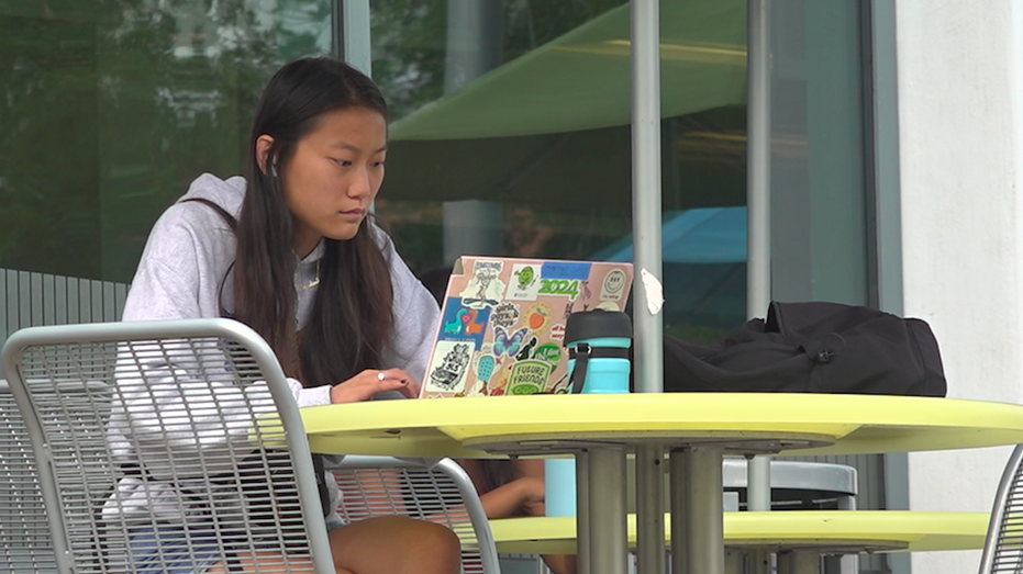 Female student sits at table outside working on laptop