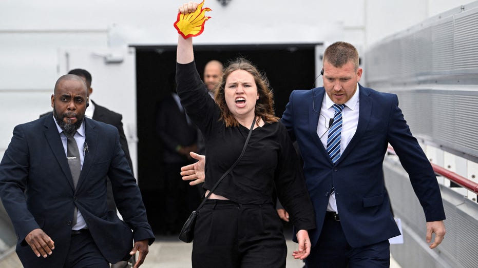 Security personnel escort an angry climate protester away from Shell's shareholder meeting as she raises Shell's logo in her fist