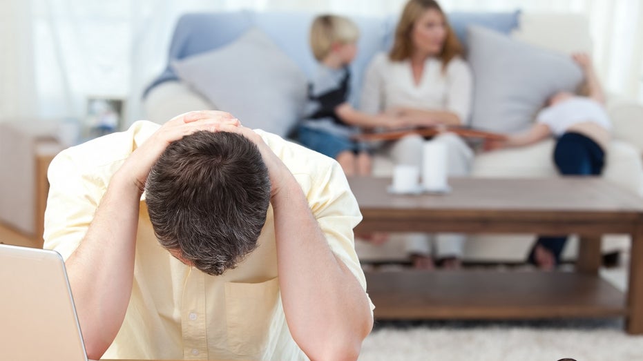 man stressed calculating bills with family behind him