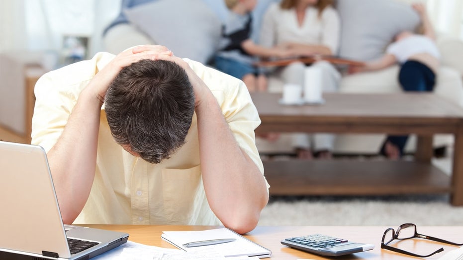 man stressed calculating bills with family behind him