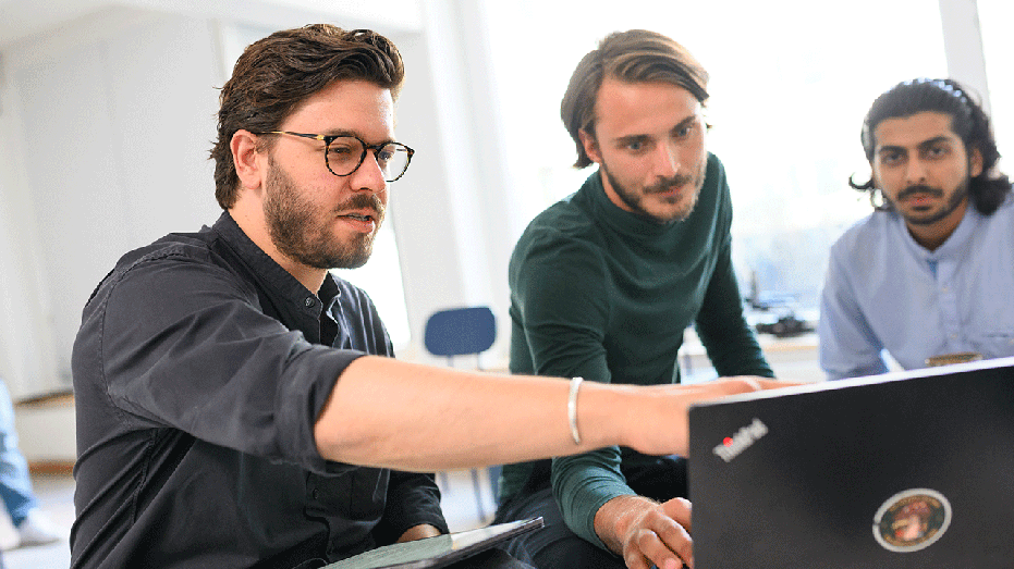 Three men standing around a computer