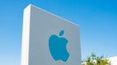 Close-up of blue logo on sign with facade of headquarters buildings in background near the headquarters of Apple Computers in the Silicon Valley, Cupertino, California, August 26, 2018. 