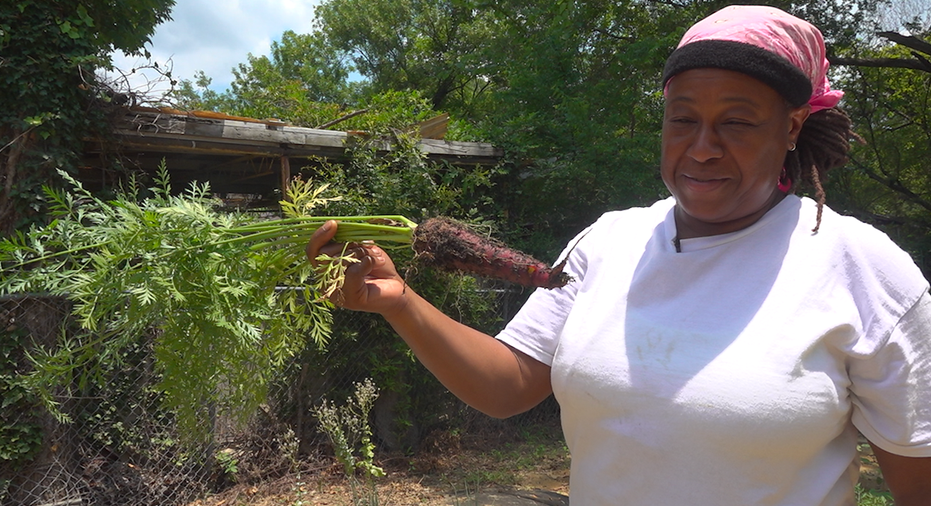 Woman in gardening clothes smiling holding up carrot pulled from the ground