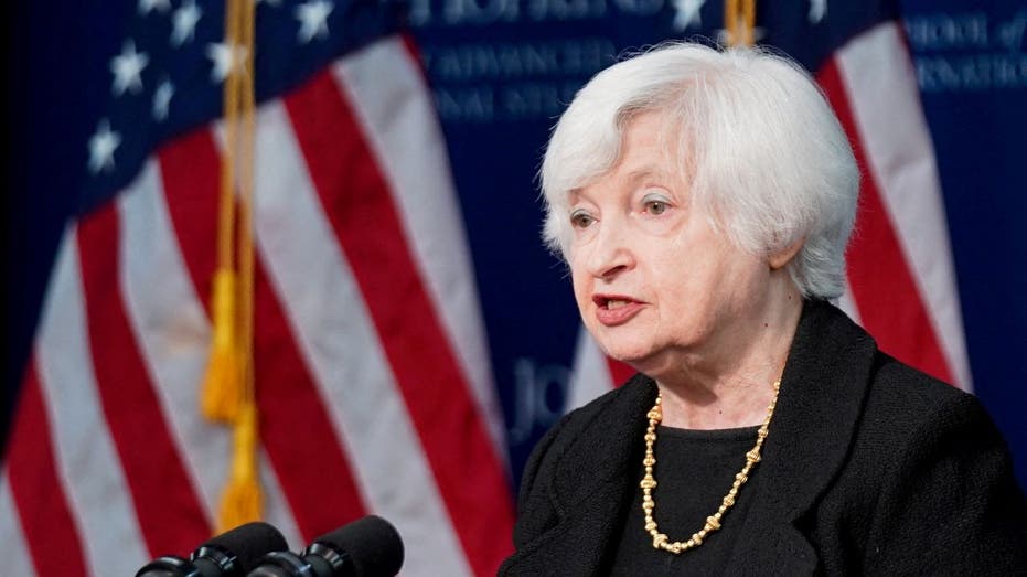 Janet Yellen at microphone with US flags behind her