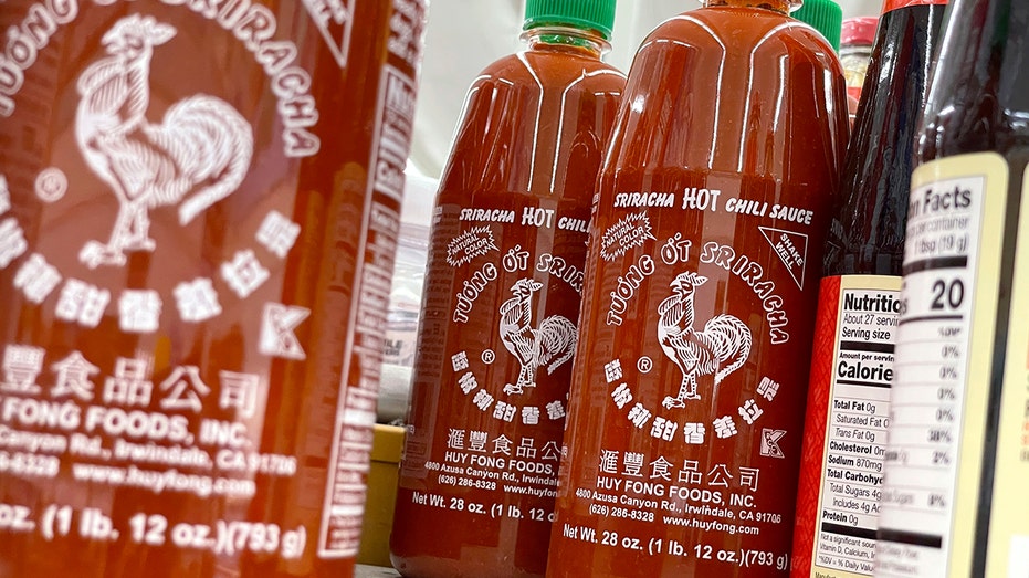 Huy Fong Foods sriracha bottles arranged on a table next to soy sauce bottles.