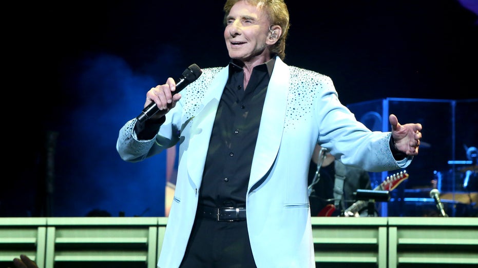 Barry Manilow performs on stage in a light blue jacket