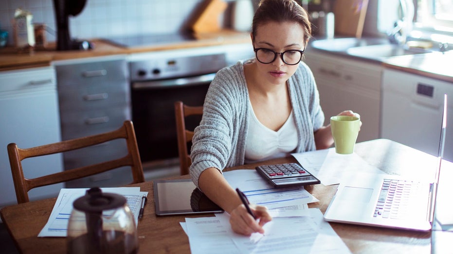 young woman paying bills at kitchen table