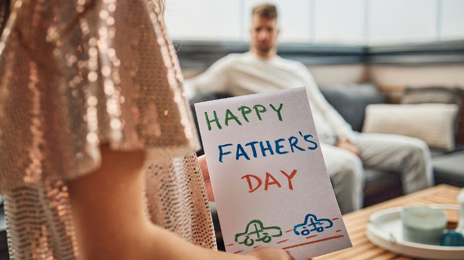 Woman holds Father's Day card as she preps to give it to a man.