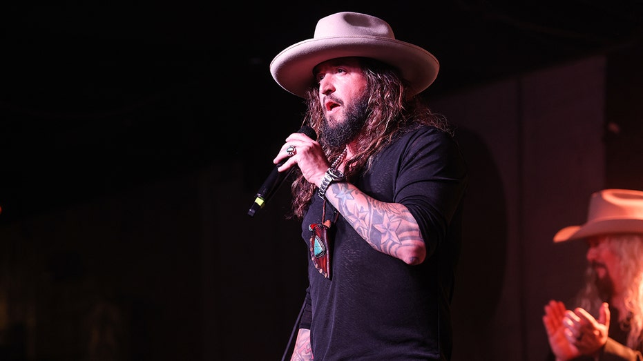 Scooter Brown holds a microphone on stage during concert