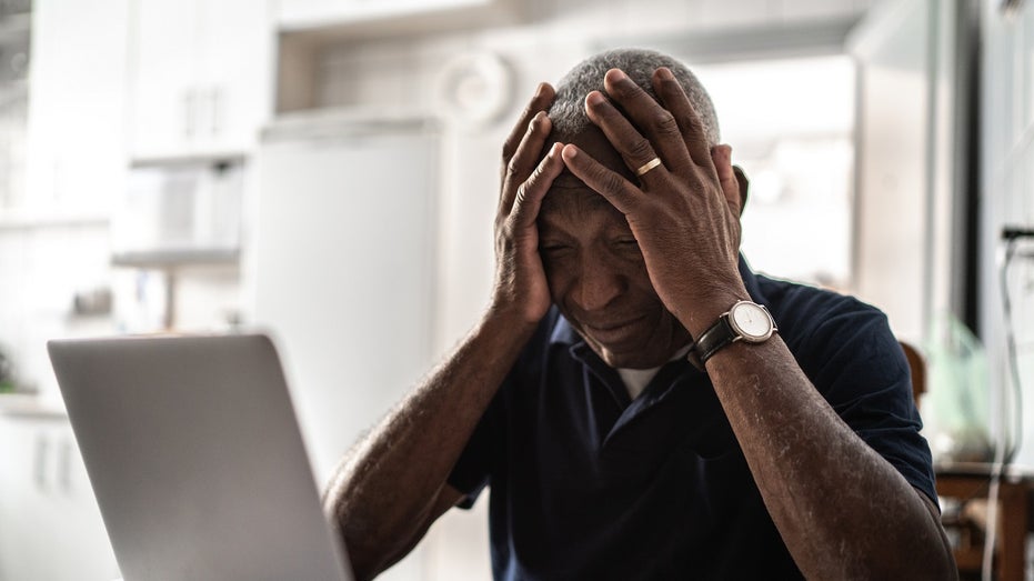 older man head in hands in front of computer