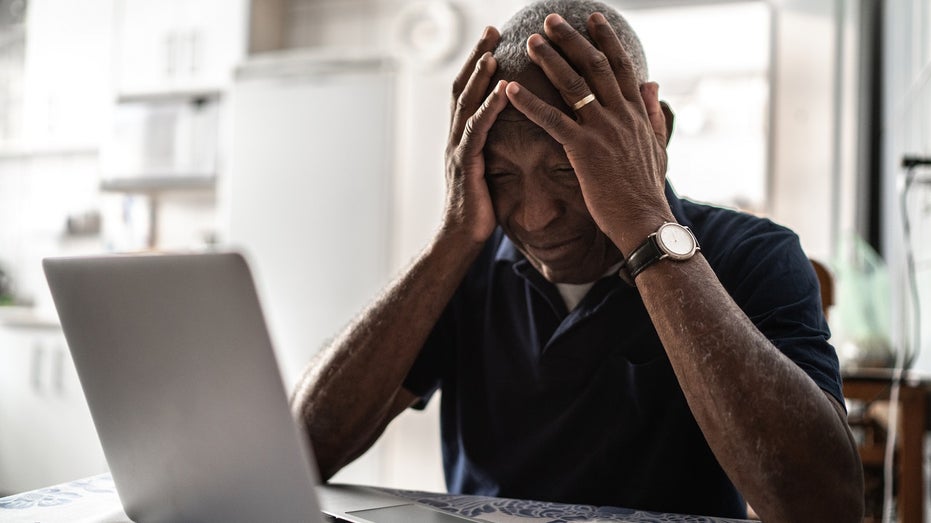 older man head in hands in front of computer