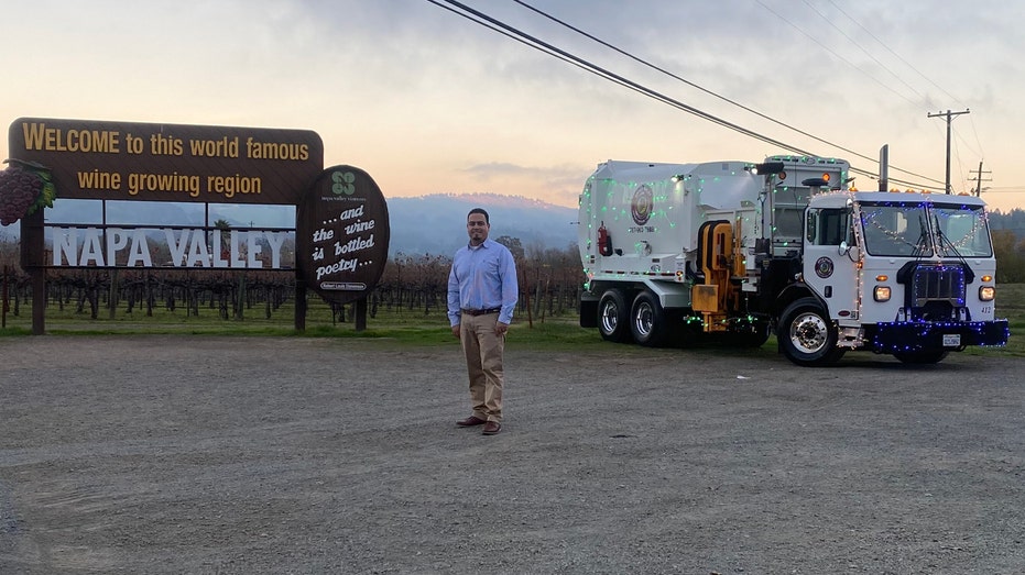 Jose Garibay poses alongside garbage truck decorated with Christmas lights in Napa Valley