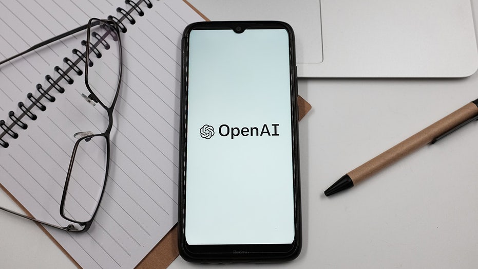 OpenAI logo seen on phone screen around pieces of paper