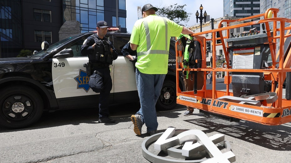 San Francisco police talk to a worker who was removing letters from the Twitter sign