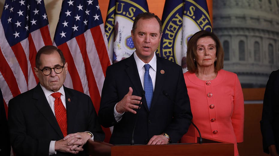 Adam Schiff speaks at podium, Nancy Pelosi stands behind him