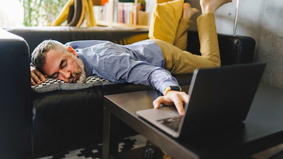 man sleeping with hand on laptop keyboard at home