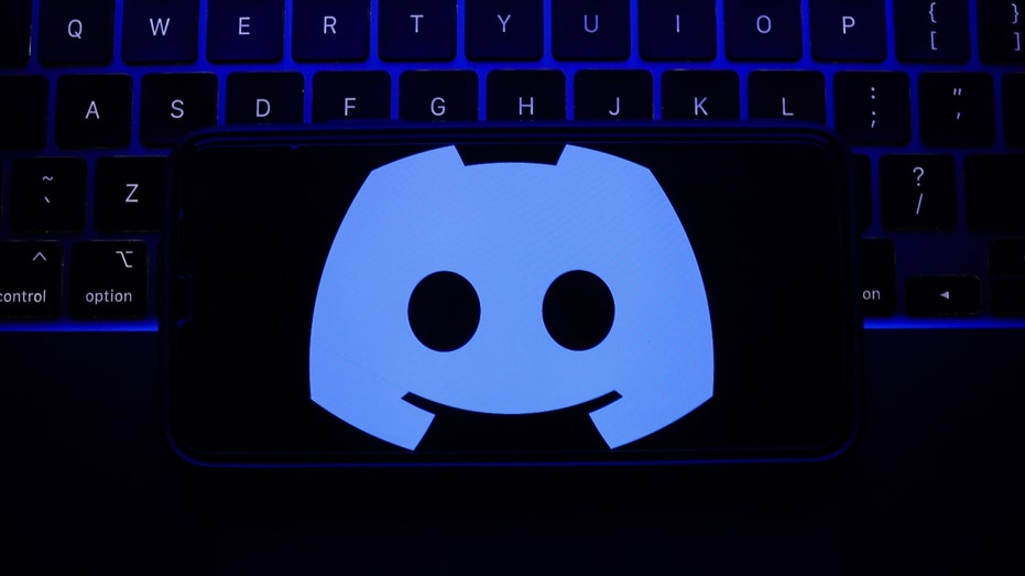 A laptop keyboard and Discord logo displayed on a phone screen