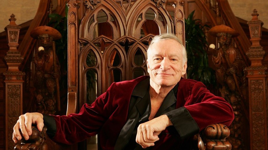 A close-up of Hugh Hefner sitting on a throne wearing a red and black robe