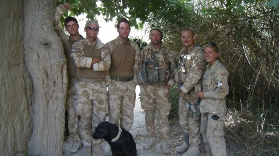 Kelsi Sheren surrounded by those in the military posing with a black dog
