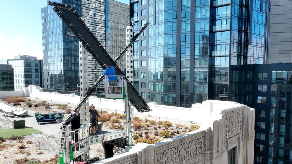 Workers start to dismantle a large X logo