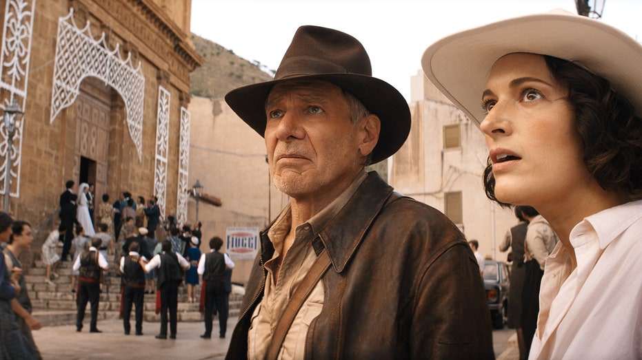 Harrison Ford as Indiana Jones looks up in his cowboy hat as Phoebe Waller-Bridge looks behind him as Helena Shaw