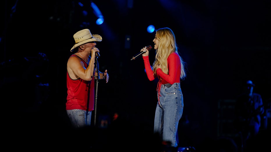 Kenny Chesney and Kelsea Ballerini wear matching red shirts while singing on stage
