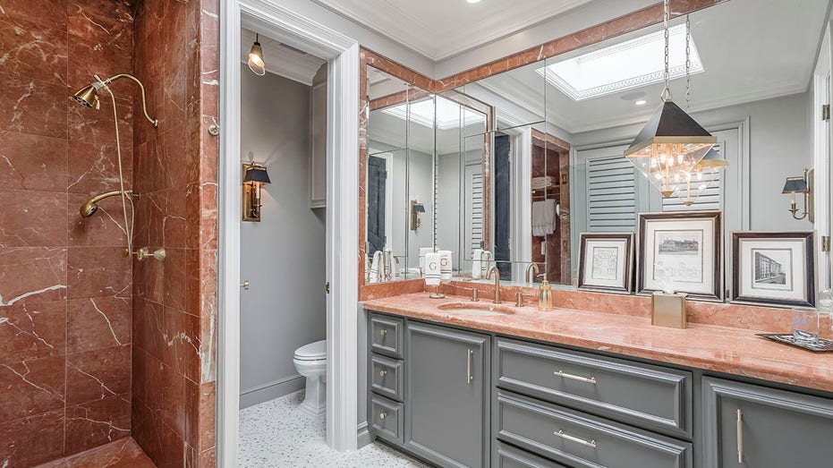 Bathroom that shows grey cabinets and an orange stone, orange stone shower, and toilet hidden behind a wall